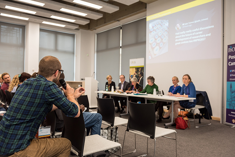 Male postdoc asking a question to a panel at a career development conference