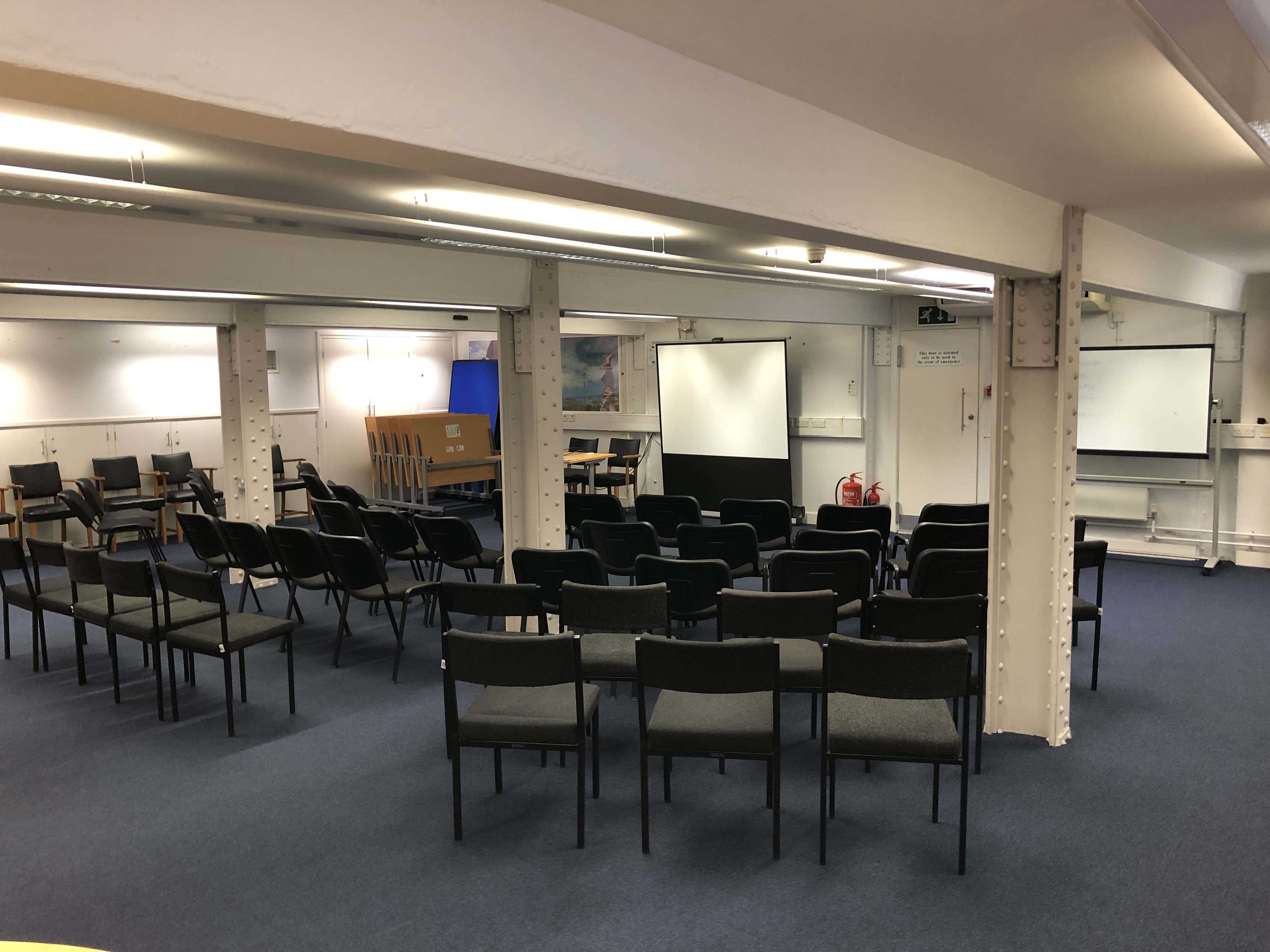 Photograph showing the lecture-style layout of the Eastwood Room - a room with five rows of chairs facing a projector screen on the end wall.