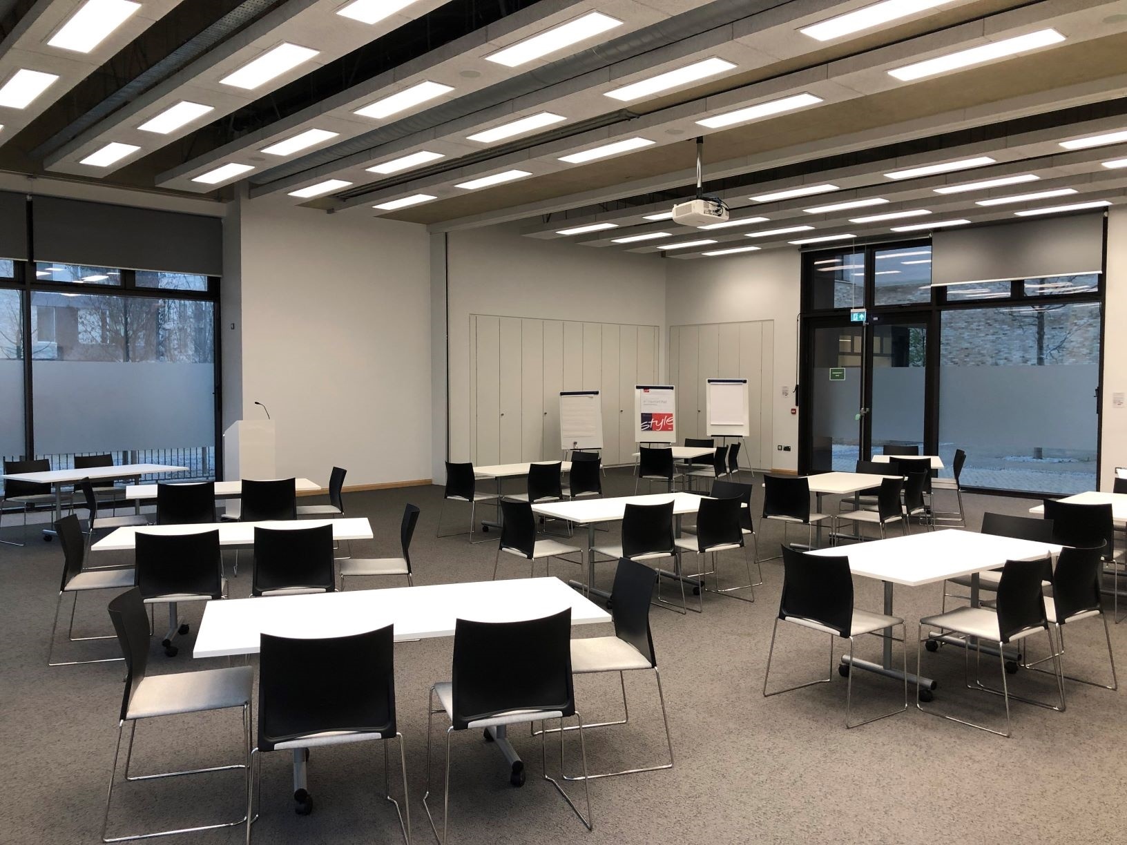 Photograph showing the workshop-style layout of Sanders Hall - a room with twelve tables each with four chairs around them.