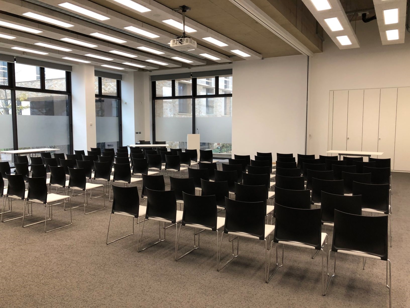 Sanders Hall lecture layout (wall open) Photograph showing the lecture-style layout of Sanders Hall - a room with seven rows of chairs facing a lectern and projector screen on the end wall.