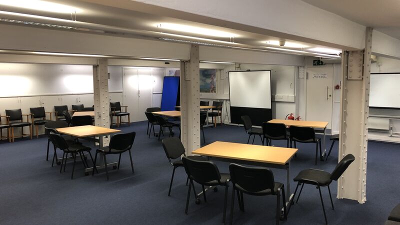 Photograph showing the workshop-style layout of the Eastwood Room - a room with five tables each with four chairs around them.