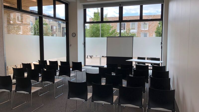 Photograph showing the lecture-style layout of the Multi-Function Space - a room with four rows of chairs facing a projector screen on the end wall.