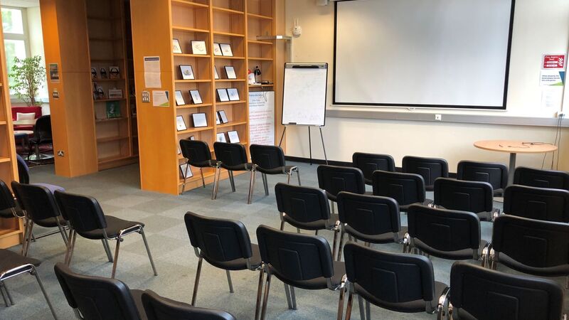 Photograph showing the lecture-style layout of the Newman Library - a room with five rows of chairs facing a projector screen on the end wall.